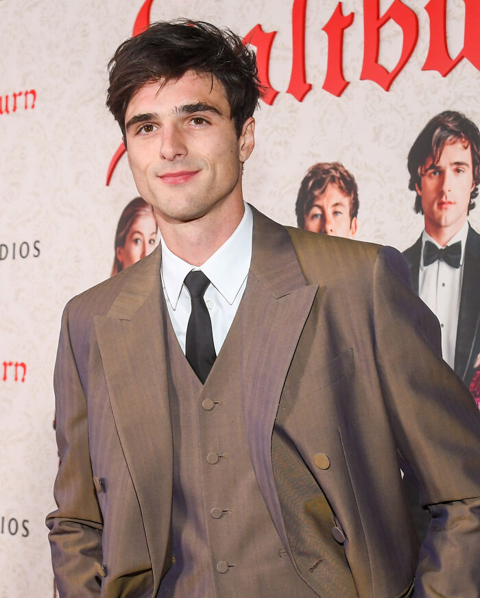Young man dressed in a brown suit and black tie, posing confidently at an event for most handsome man in the world 2025.