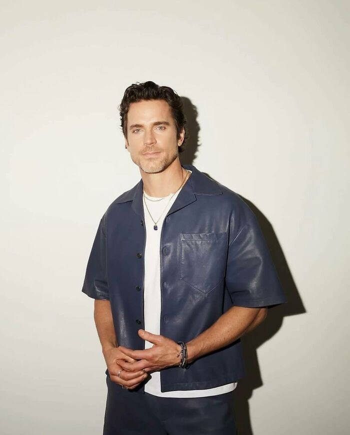 Man with dark hair wearing a navy blue shirt and white tee posing confidently, representing most handsome man in world 2025.