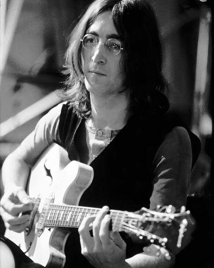Black and white photo of a musician playing guitar, representing people who left a mark in the music industry.