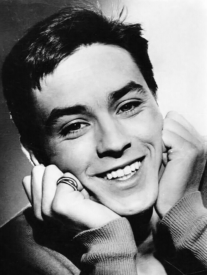 Black and white close-up of a smiling young man, representing people who left a mark in the movie and music industries.