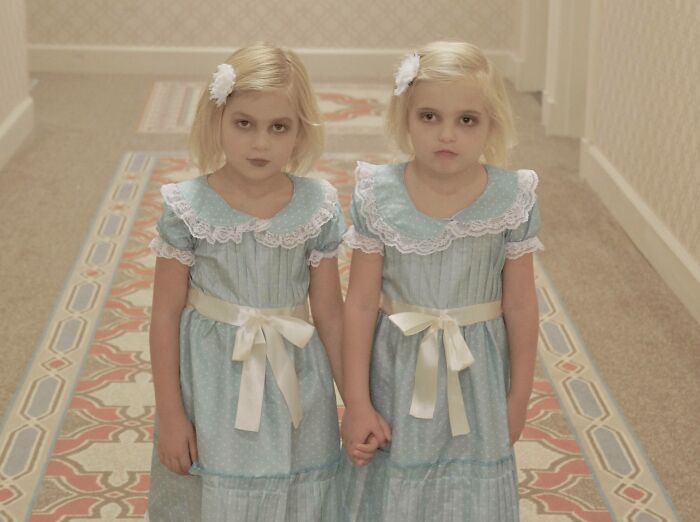 Two girls in matching blue dresses holding hands in a hallway wearing amazing kids Halloween costume ideas.