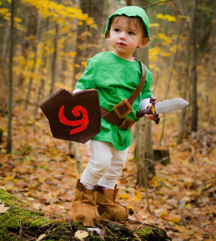 Toddler in creative kids Halloween costume ideas dressed as a fantasy warrior with shield and sword in a forest setting.