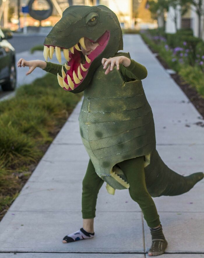 Child in a creative dinosaur Halloween costume on a sidewalk, showcasing one of the amazing kids' Halloween costume ideas.