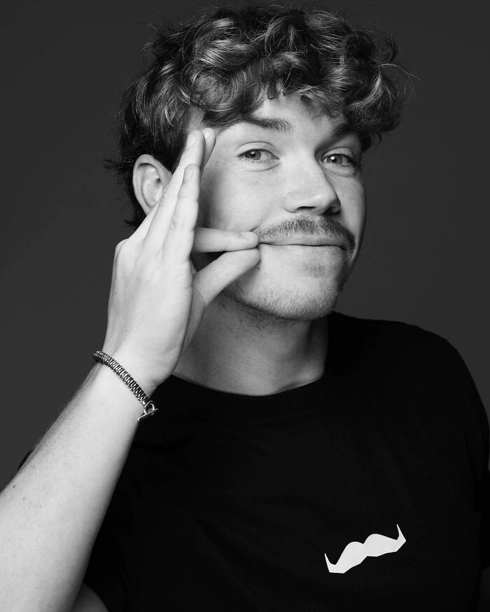 Young man with curly hair and mustache posing confidently, perfect example of most handsome man in the world 2025