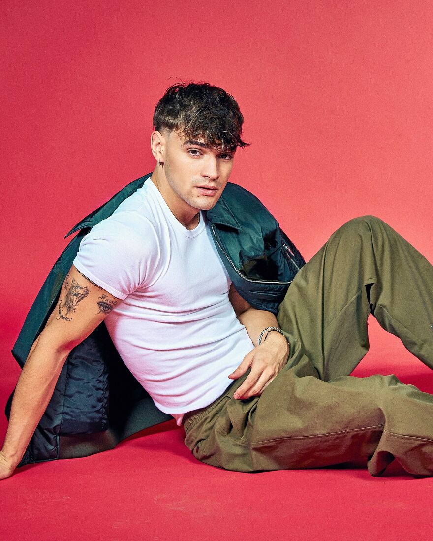 Gabriel Guevara with tattoos and a green jacket over a white shirt posing on red background, most handsome man in the world 2025.