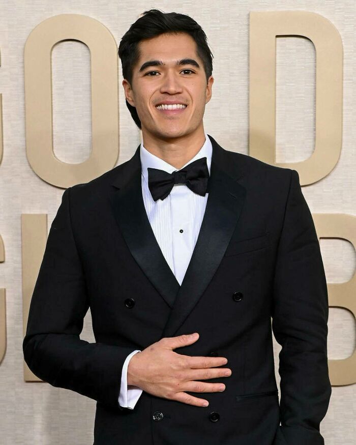 Young man dressed in black tuxedo and bow tie, smiling confidently at an elegant event for most handsome man in the world.