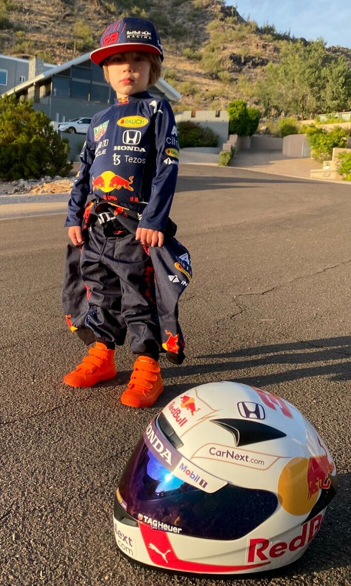 Young child in a detailed racing driver costume with helmet on ground, showcasing amazing kids Halloween costume ideas.