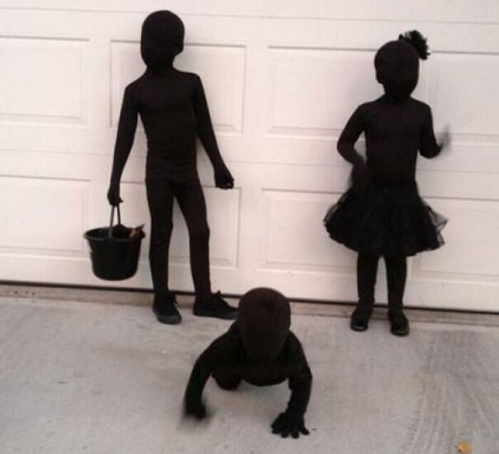 Three kids in all-black Halloween costumes posing outside a garage as part of amazing kids' Halloween costume ideas.