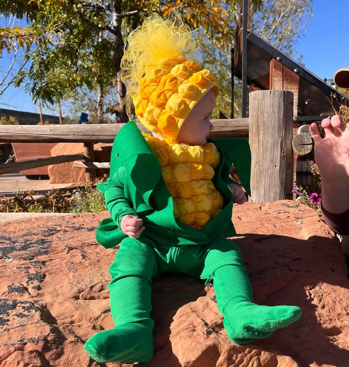Toddler in a bright green and yellow Halloween costume sitting on a rock, showcasing amazing kids Halloween costume ideas.