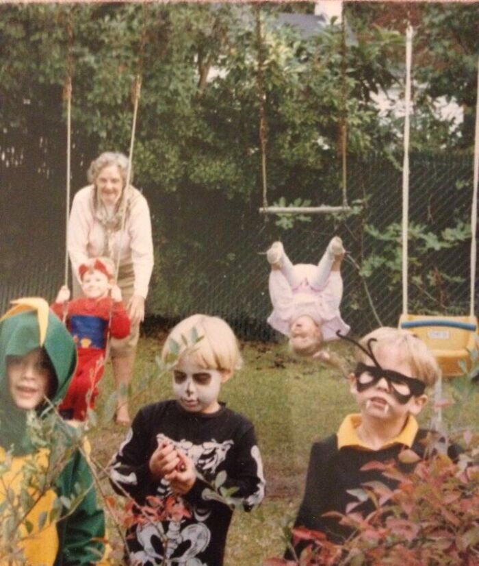 Children in Halloween costumes with an upside-down toddler on a swing in a family photo gone awkward.