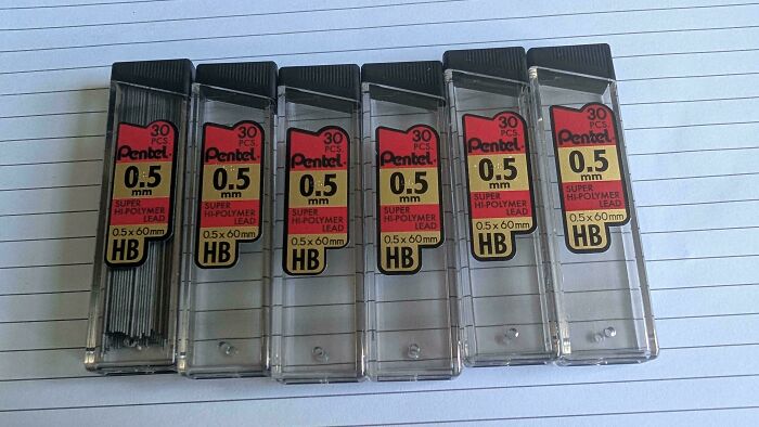 Six identical Pentel 0.5 mm HB lead refill cases lined up on lined paper, illustrating careless online shopping fails.