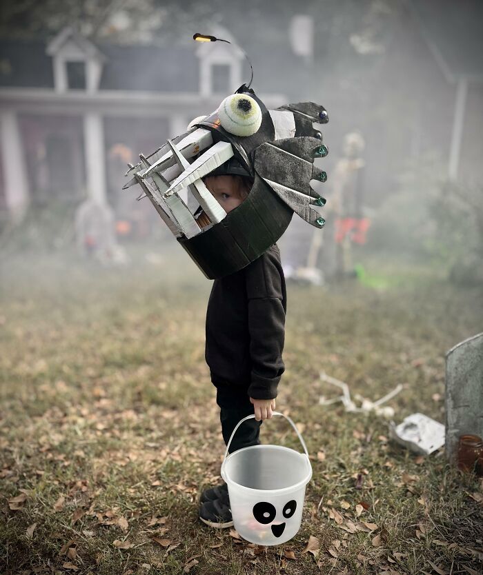 Child wearing a creative anglerfish Halloween costume holding a ghost-themed bucket in a spooky outdoor setting for kids' Halloween costume ideas.