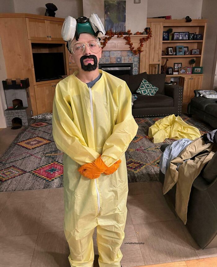 Child in a creative kids Halloween costume idea wearing a yellow hazmat suit with gloves and protective goggles indoors.