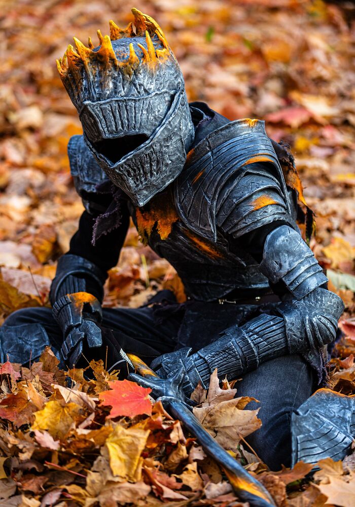 Child in an armored Halloween costume with flame details sitting among autumn leaves for kids Halloween costume ideas.