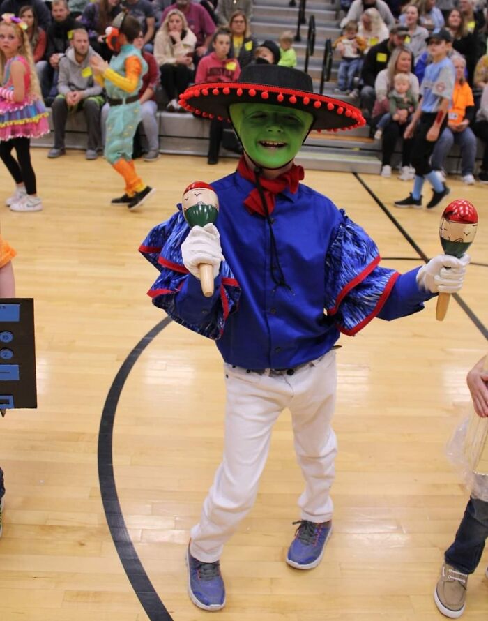 Child in colorful Halloween costume with face paint and hat holding maracas at a kids Halloween costume event