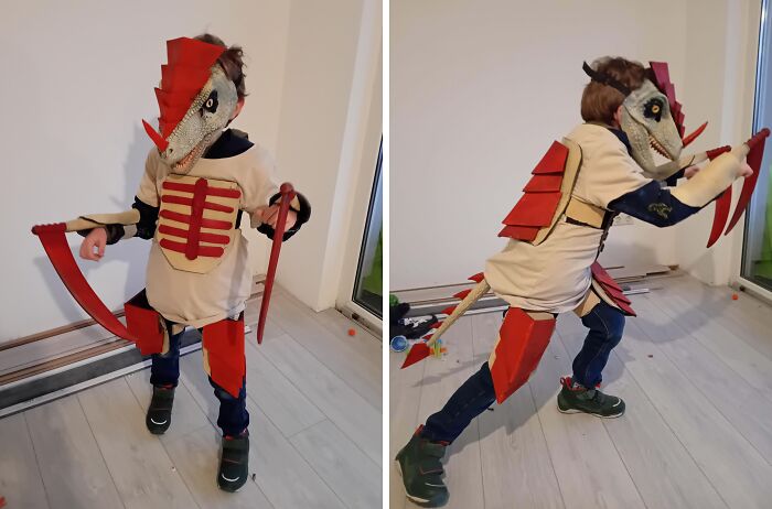 Child wearing an amazing kids Halloween costume resembling a dinosaur with red spikes and claws, posing indoors on a wooden floor.