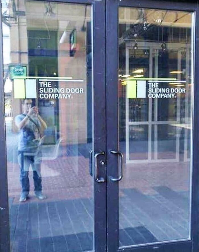 Glass doors with handles and signs for a sliding door company, humorously contradicting the business name.