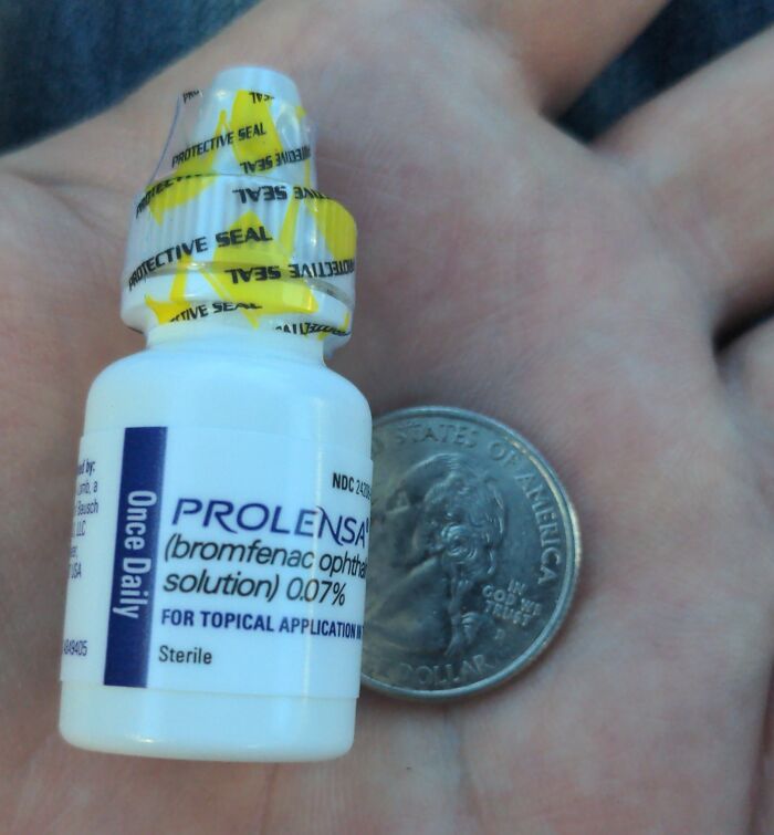 Small bottle of eye medication held next to a US quarter, illustrating the harsh realities of American healthcare costs.