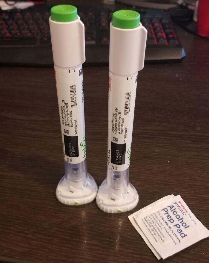 Two injectable medication pens and an alcohol prep pad on a wooden surface highlighting American healthcare realities.