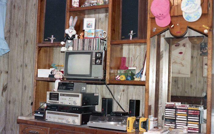 Vintage 1980s entertainment setup with CRT TV, cassette tapes, stereo system, and retro collectibles in a wood-paneled room.