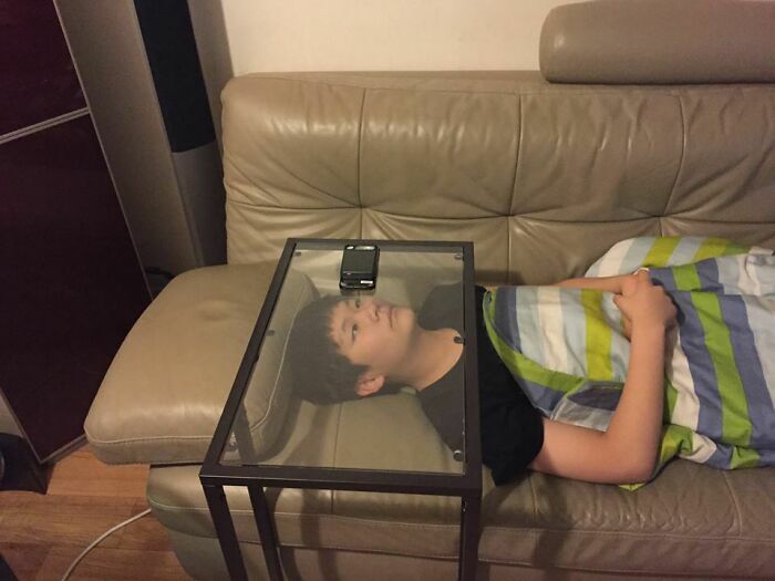 Boy laying on couch with a glass table over his head holding a phone as a creative kids invention surprise for parents.