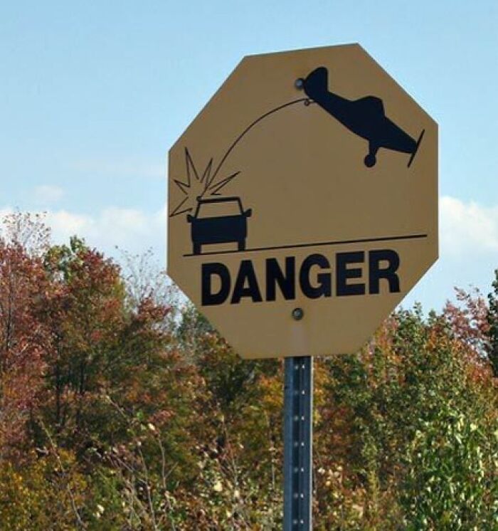 Confusing road sign showing a car crashing into an upside-down airplane with the word danger, highlighting unclear road signs.
