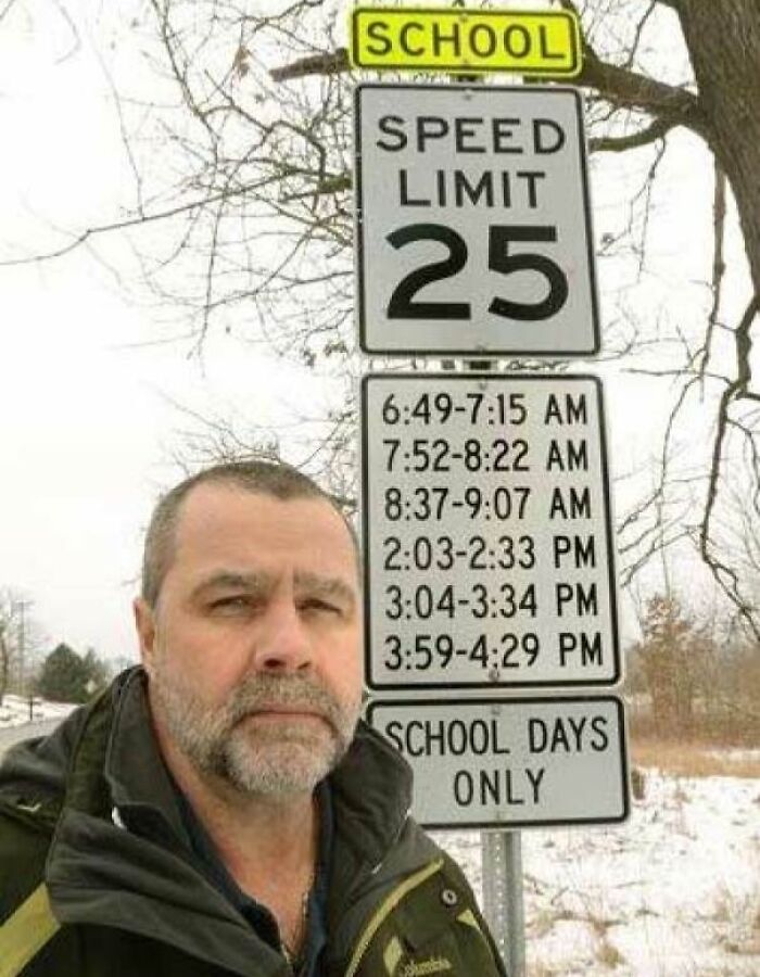 Man standing near confusing school zone speed limit road sign with multiple time intervals on a winter day