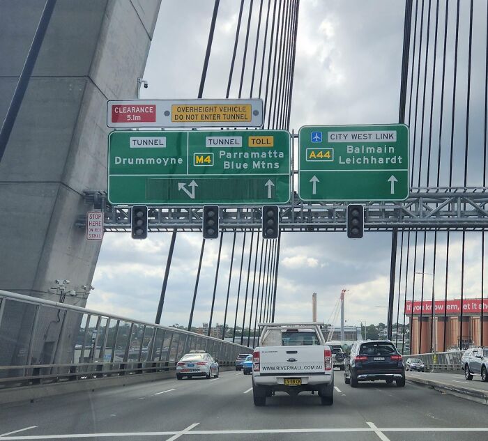 Confusing road signs for tunnels, tolls, and city directions causing drivers to ignore GPS instructions on a busy bridge.