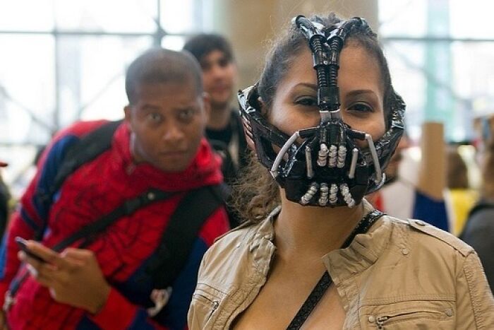 Woman wearing a detailed mask with a man in a Spiderman costume photobombing, capturing a perfect photobomb moment.