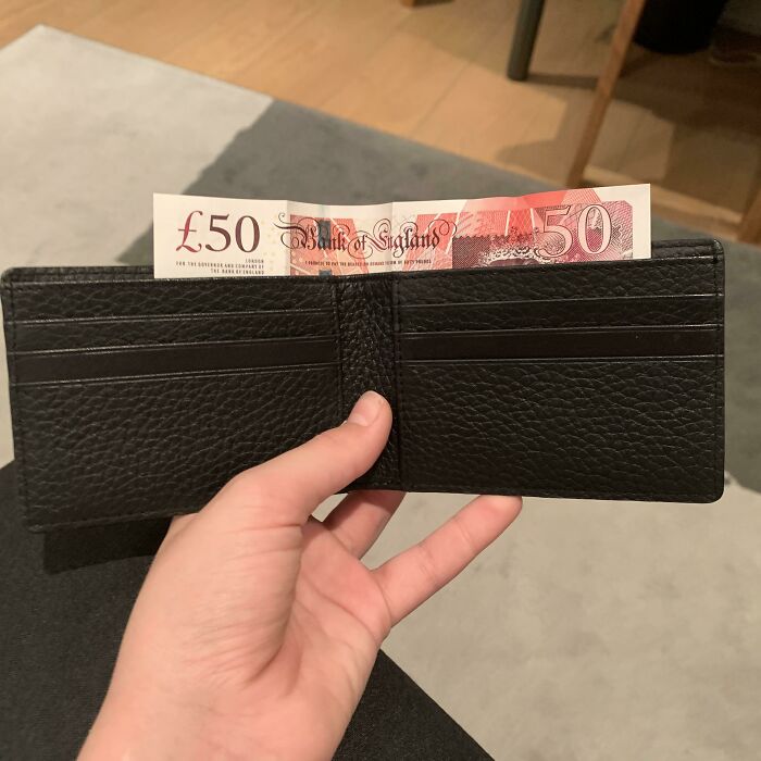 Hand holding a black wallet with a £50 note sticking out, illustrating mildly infuriating things testing patience.