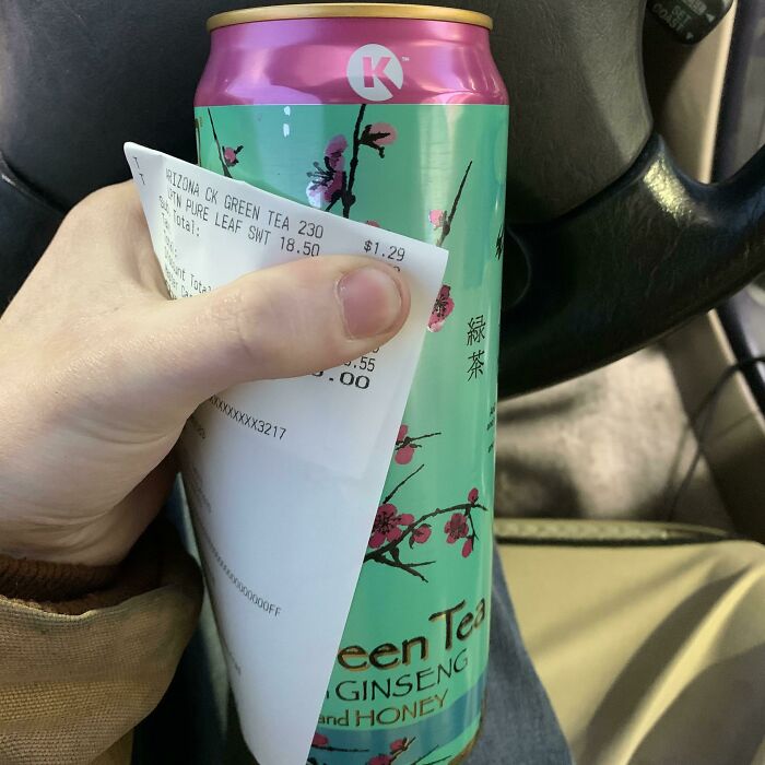Hand holding a can of green tea with receipt partially covering the label, showing a mildly infuriating packaging design.