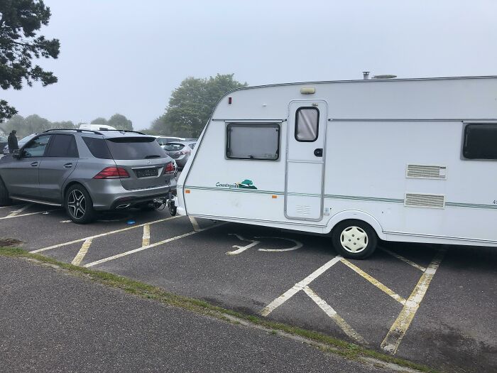 Car towing camper parked across multiple spaces, a mildly infuriating thing testing people's patience in parking lots.
