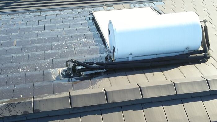 Roof with a white cylindrical tank and black pipes, showing a mildly infuriating misalignment on shingles and installation.