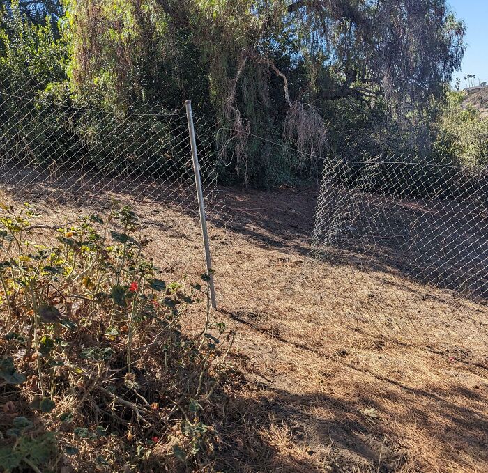 Chain link fence with a bent post and sagging wire creating a mildly infuriating scene that tests patience outdoors.