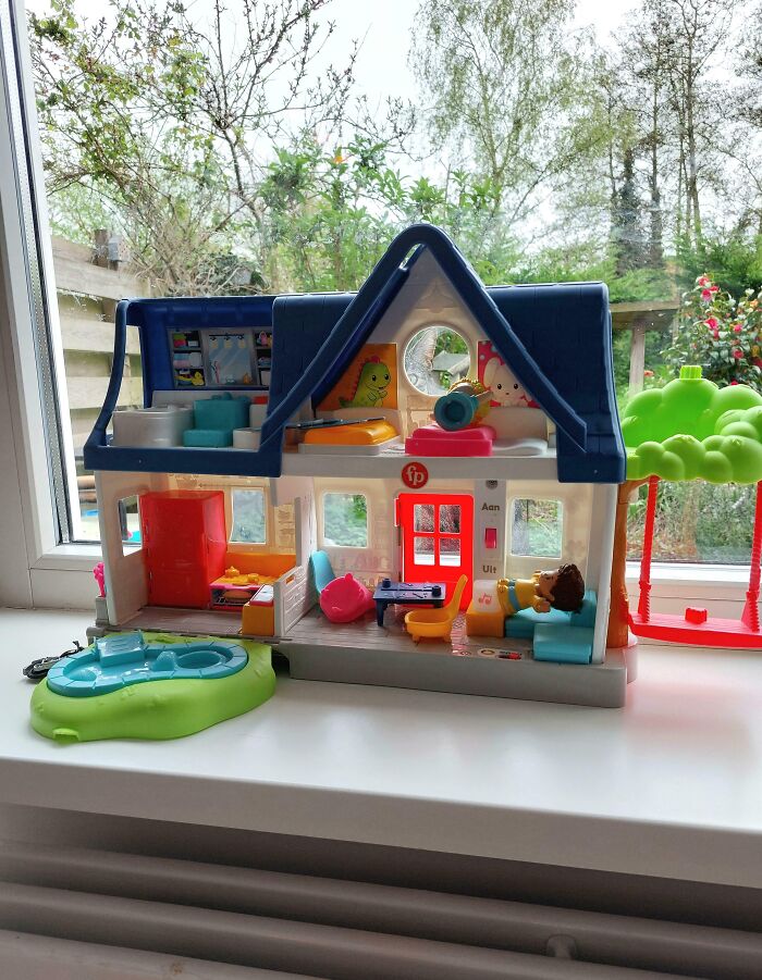 Toy dollhouse setup on a windowsill with colorful furniture and a small toy figure blending into the background.