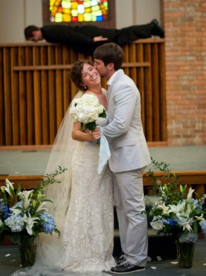Bride and groom share a kiss at wedding while a photobomb behind them creates a total disaster or absolute perfection moment.