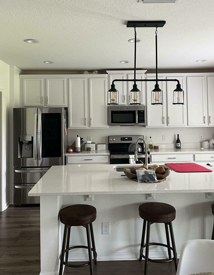 Cat blending seamlessly into the background on top of white kitchen cabinets in a modern kitchen setting.