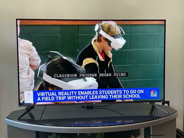 Two students wearing virtual reality headsets experiencing a field trip in a classroom setting, mildly infuriating.