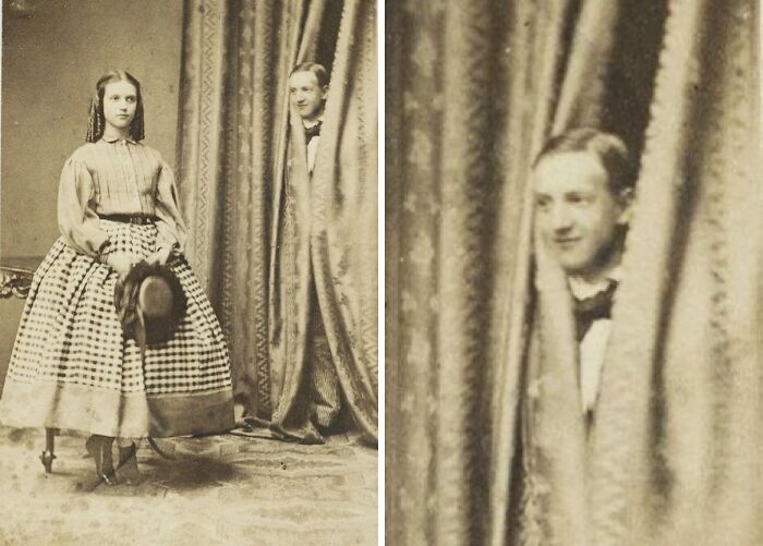 Vintage photo showing a woman posing while a man photobombs by peeking out from behind curtains, capturing a perfect photobomb moment.