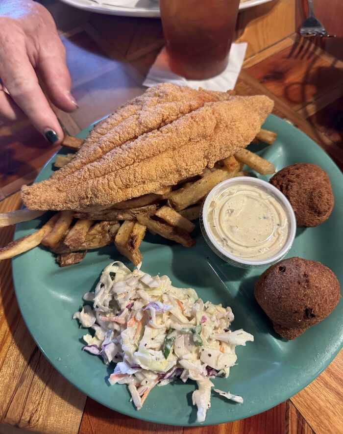 Plate with fried fish showing uneven batter that tested people's patience, served with fries, coleslaw, hush puppies, and sauce.