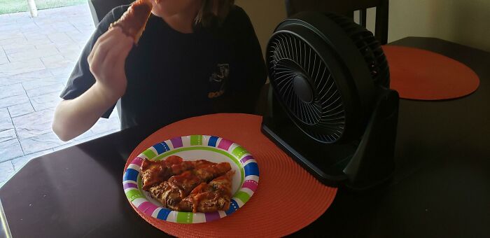 Child using a fan to cool pizza slices while eating, showcasing kids outsmarting grown-ups in an entertaining way.