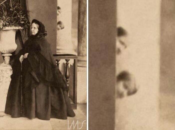 Vintage photo of a woman in a dark dress with an unexpected photobomb of two faces peeking from behind a column.