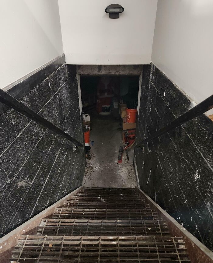 Narrow, dimly lit basement stairs with black walls leading to a cluttered, eerie storage area in unsettling worker photo.