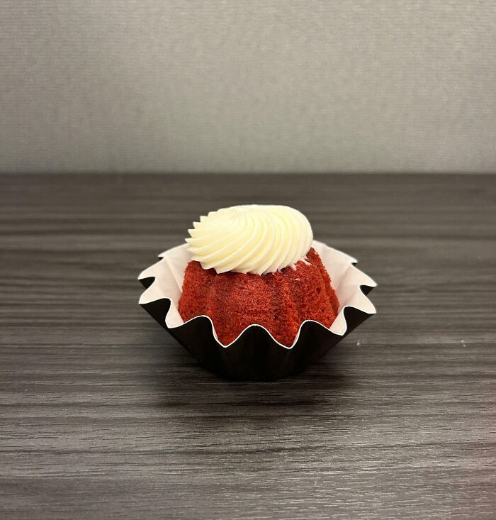 Single red velvet cupcake with white frosting in a crumpled paper liner, showcasing mildly infuriating design flaw.