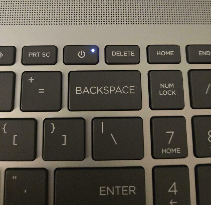 Close-up of a keyboard showing a small power button with a blue light above the large backspace key, mildly infuriating detail.