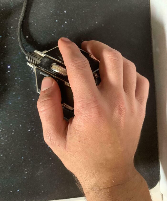 Hand gripping a gaming mouse on a black speckled mousepad, illustrating mildly infuriating things testing patience.