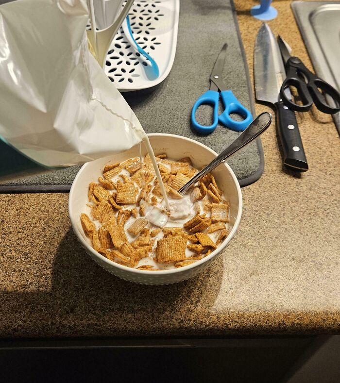 Pouring milk unevenly over cereal in a bowl, showcasing a mildly infuriating thing that tests patience.