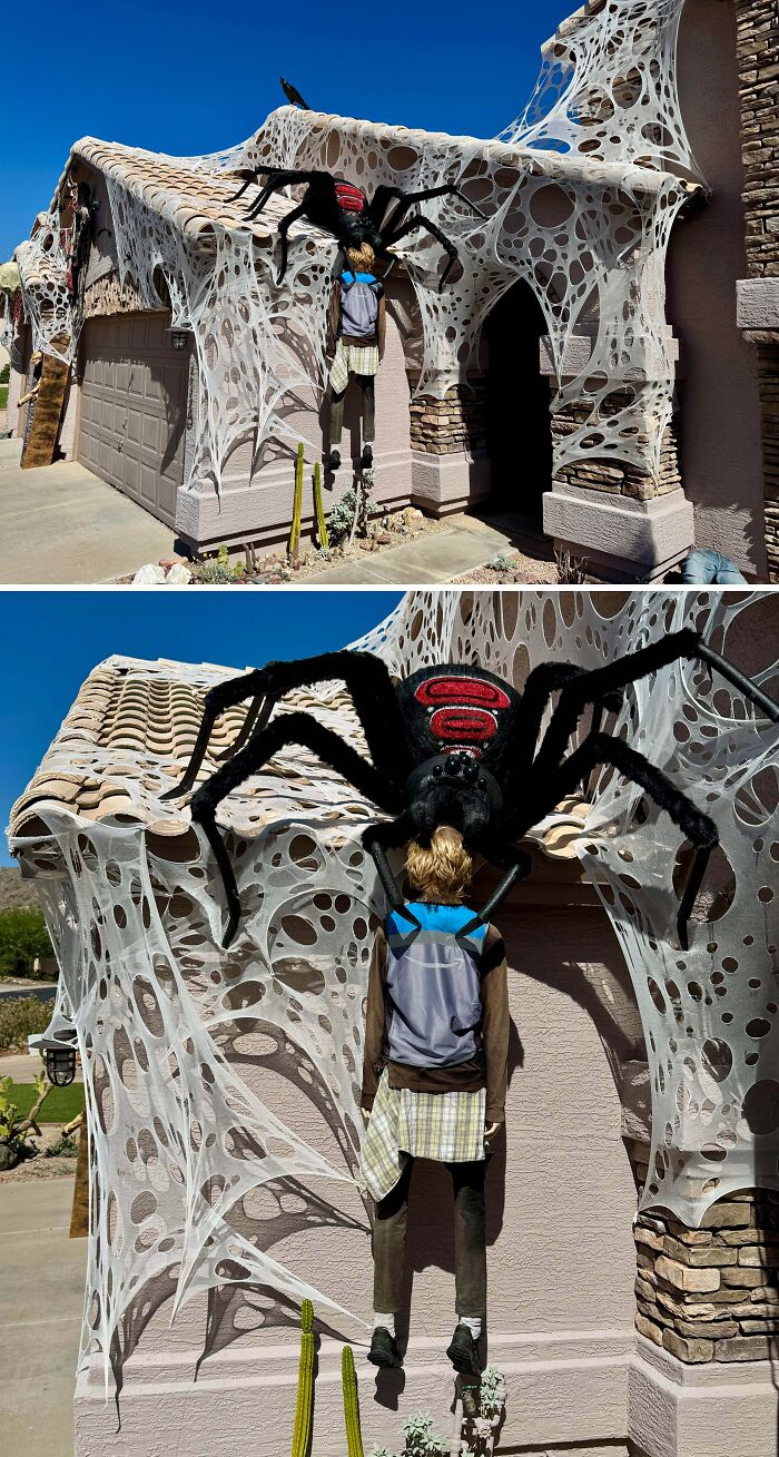Outdoor Halloween decorations with giant spider attacking a hanging dummy, covered in webbing on a suburban house facade.