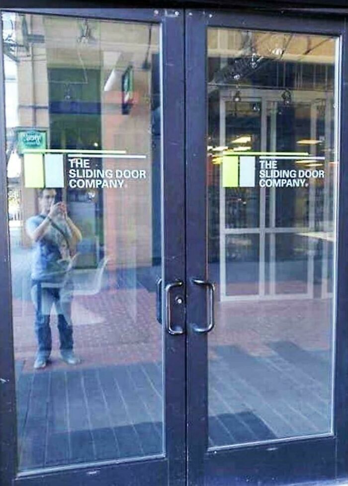 Reflection showing a person taking a photo through glass doors at the sliding door company, showcasing accidental comedy.