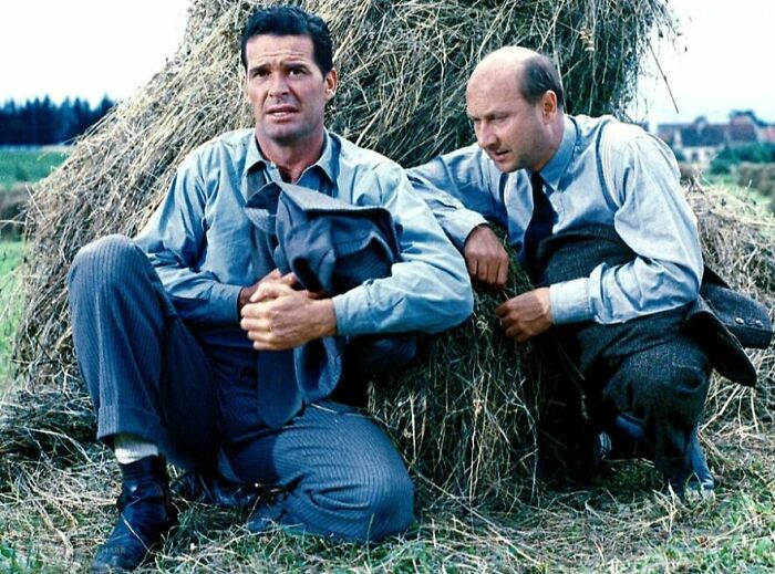 Two men in vintage clothing sitting against a haystack in a scene from movies based on true stories.